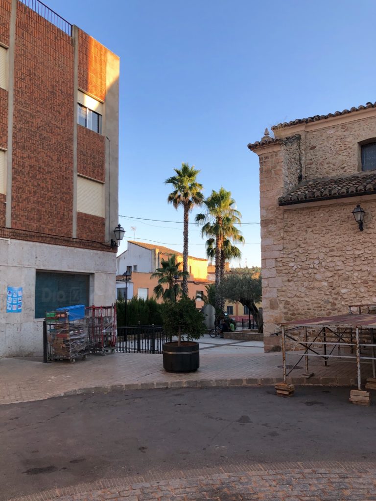 The centre of Caudete de las Fuentes, including a shop some palm trees, and the corner of a church.