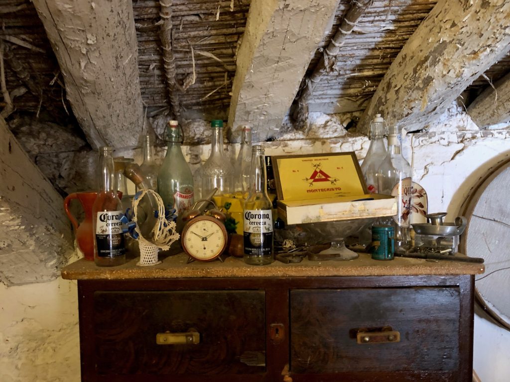 An old chest topped with glass knickknacks and hidden under the rafters of an old roof.