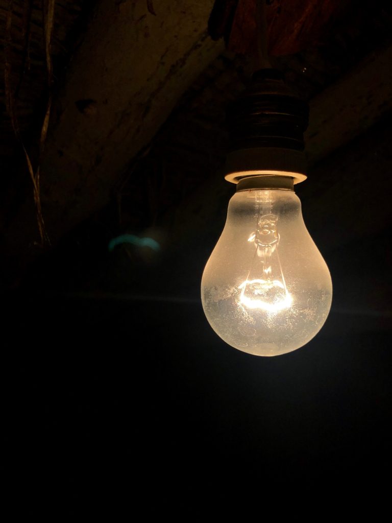 An old incandescent lightbulb burns in the loft of an old house.
