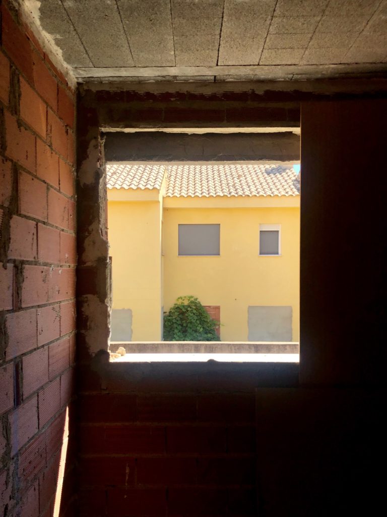 An abandoned house can be seen through the missing window of another abandoned house.
