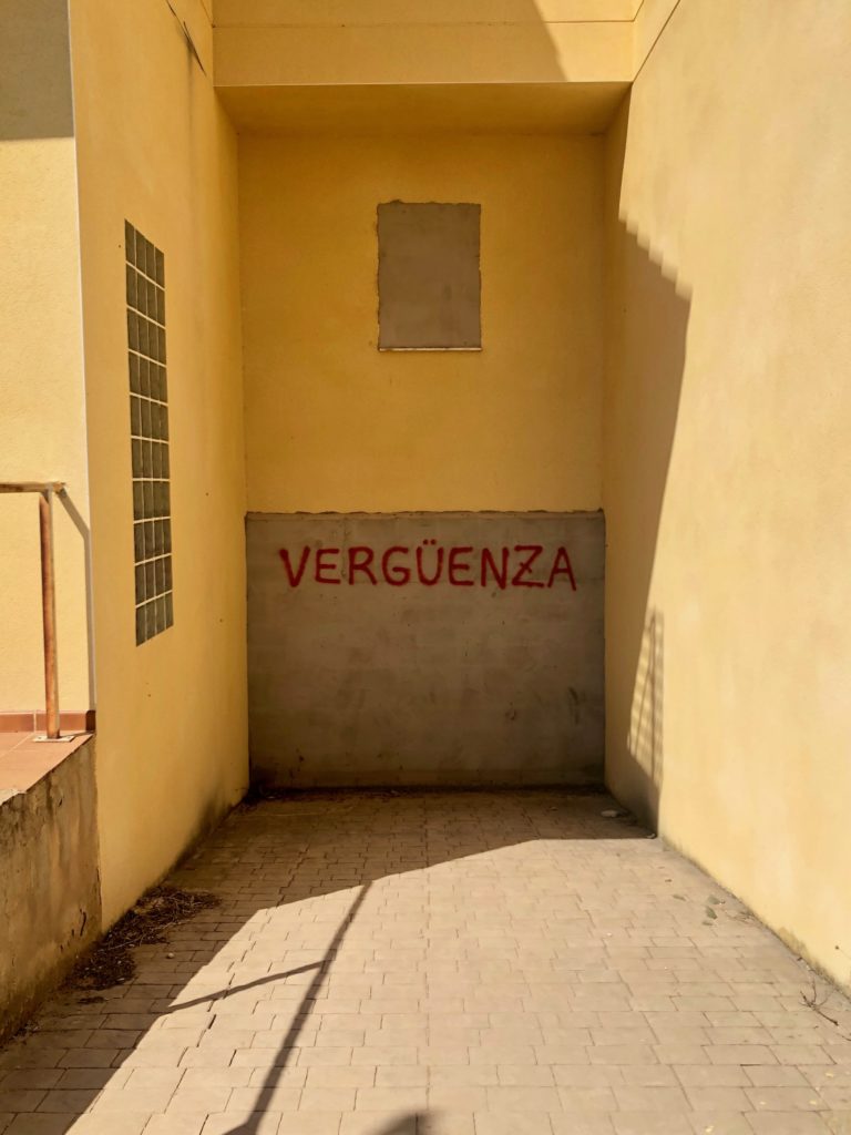 The Spanish word "vergüenza", meaning shame, is graffitied onto the blocked-up entrance to the subterranean garage of an abandoned house.