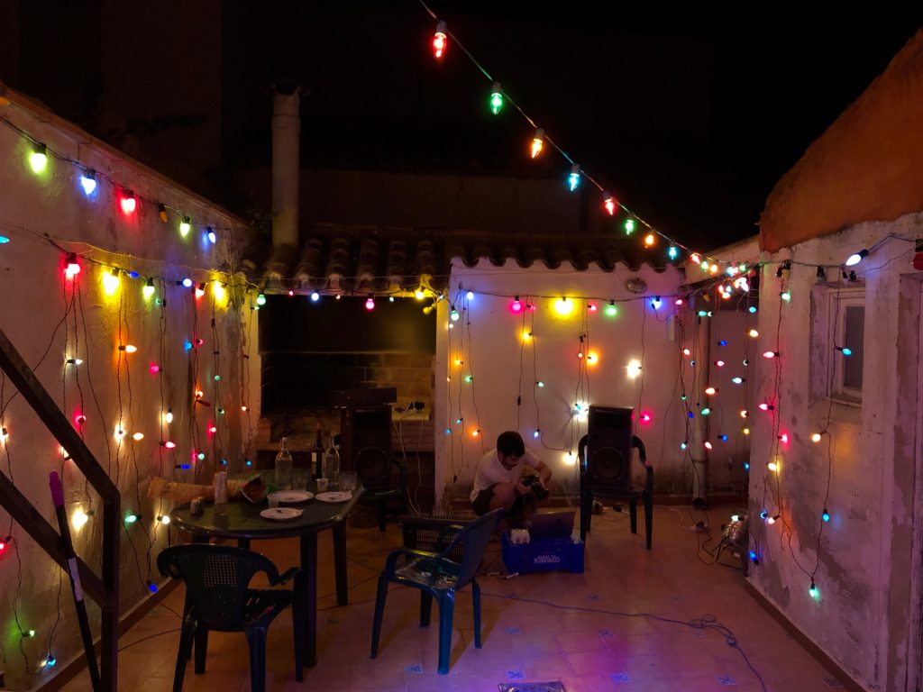 A patio at night illuminated by a web of multicoloured string lights which decorate the walls.
