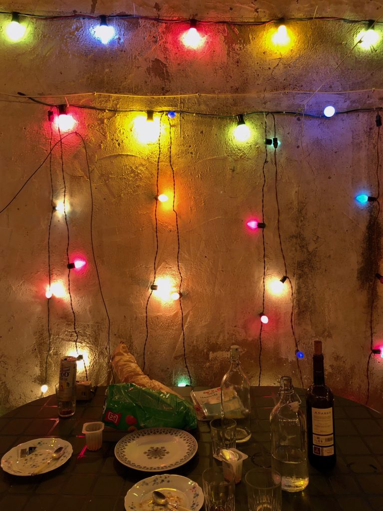 A web of lights on a wall sits behind a table littered with bottles and leftover food.