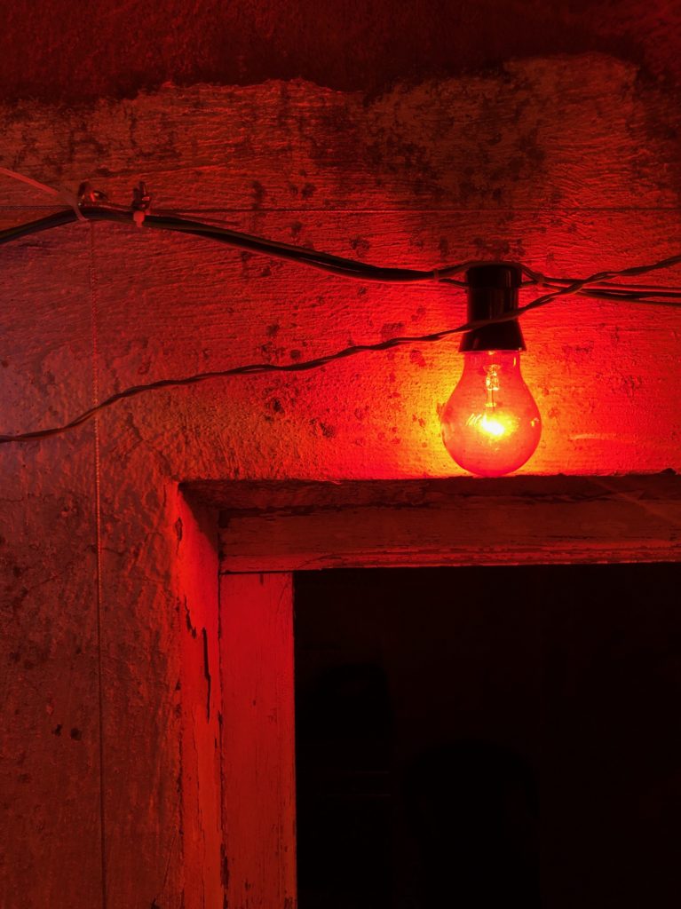 A red lightbulb against an old plaster wall and above an open doorway.
