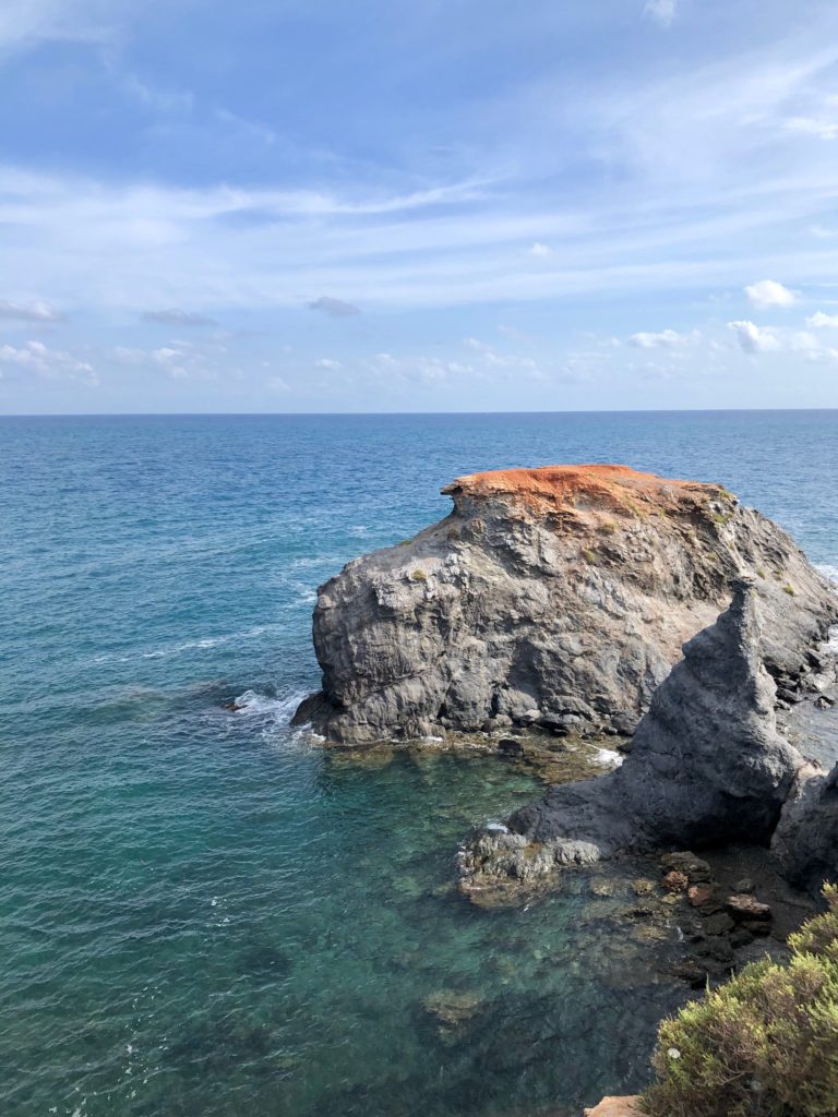A colourful rock juts out into the sea.