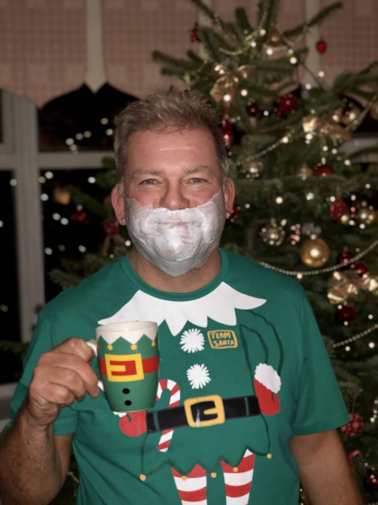 My dad with a beard of shaving foam, an elf mug and t-shirt, and our Christmas tree in the background.
