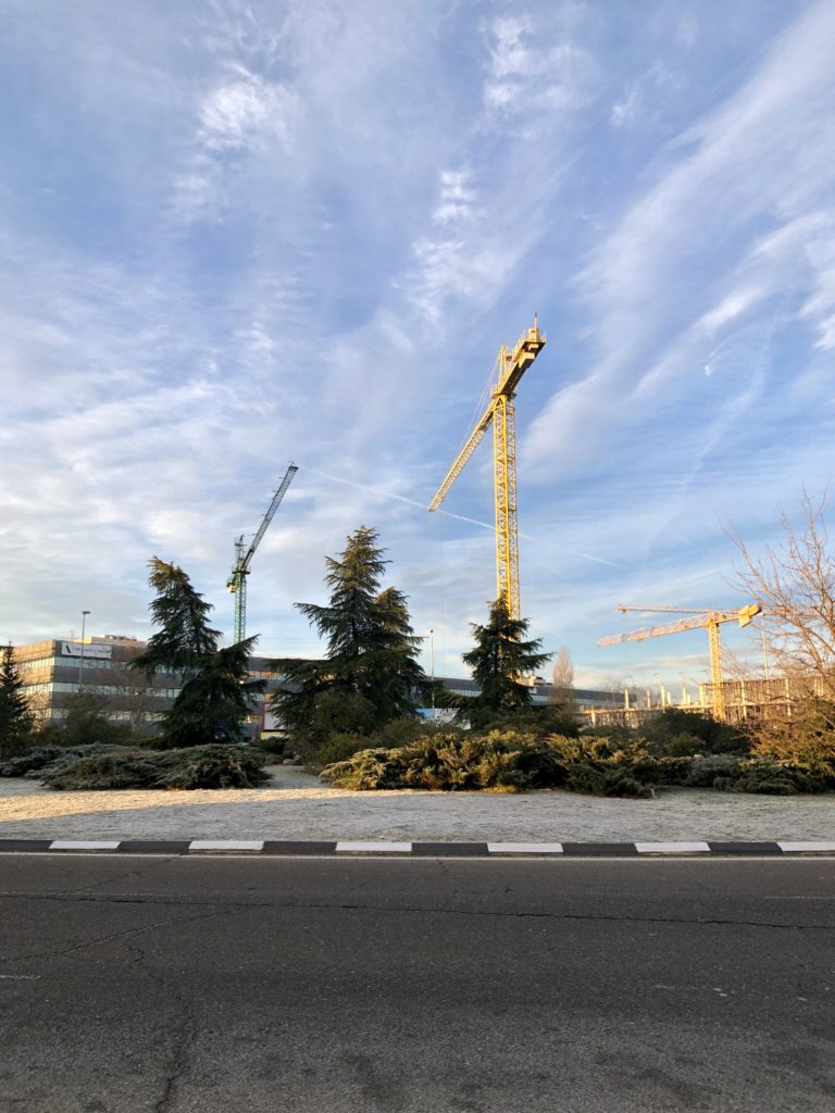 A series of cranes below the blue sky over a frosty grassy knoll.