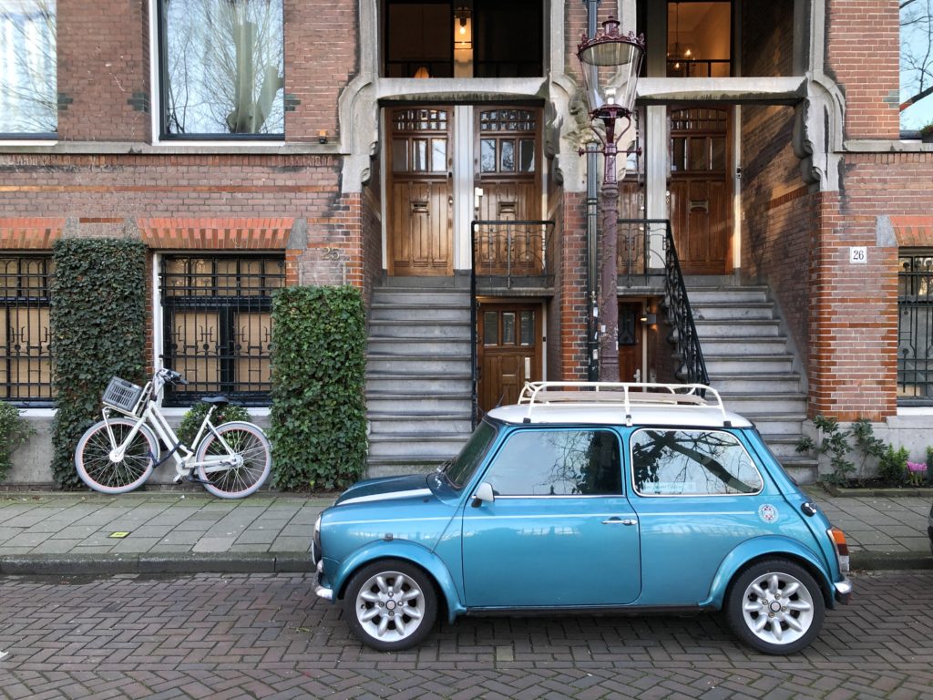 A Mini Cooper, a bicycle, and an old gas lamp in front of old red brick houses in Amsterdam.