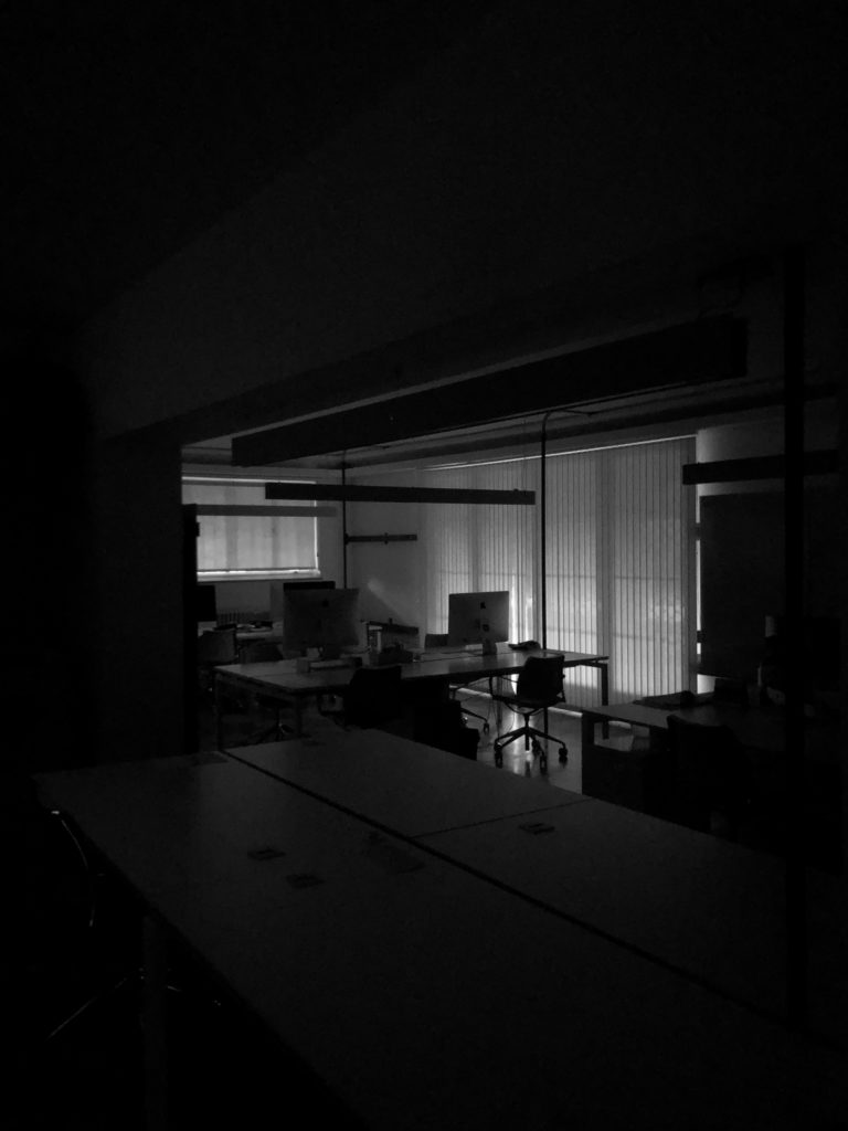 The profiles of computers are seen in a darkened office.