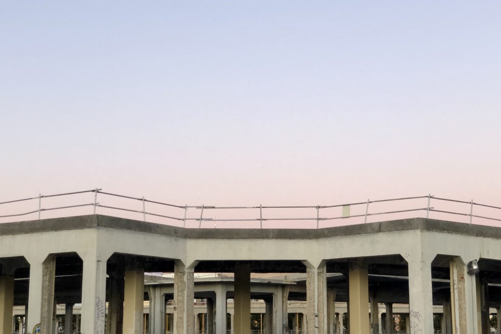 A pastel blue and pink sky sets over the concrete shell of a large structure.