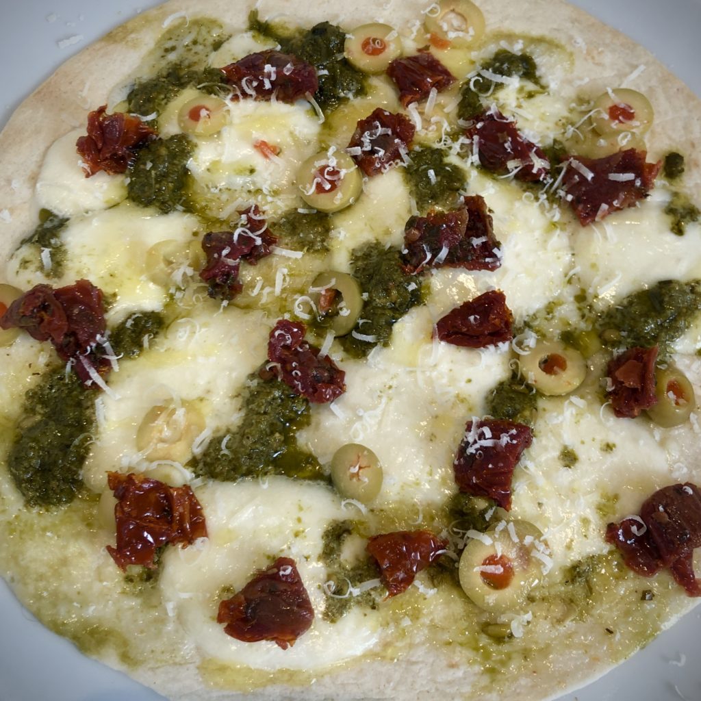 An Italian-style flatbread covered in mozzarella, pesto, dried tomato, olives, and parmesan.