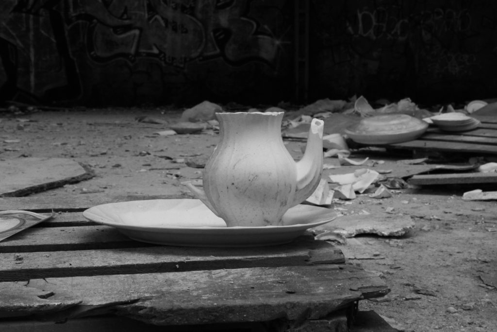 A broken ceramic teapot sita atop a wooden palette.