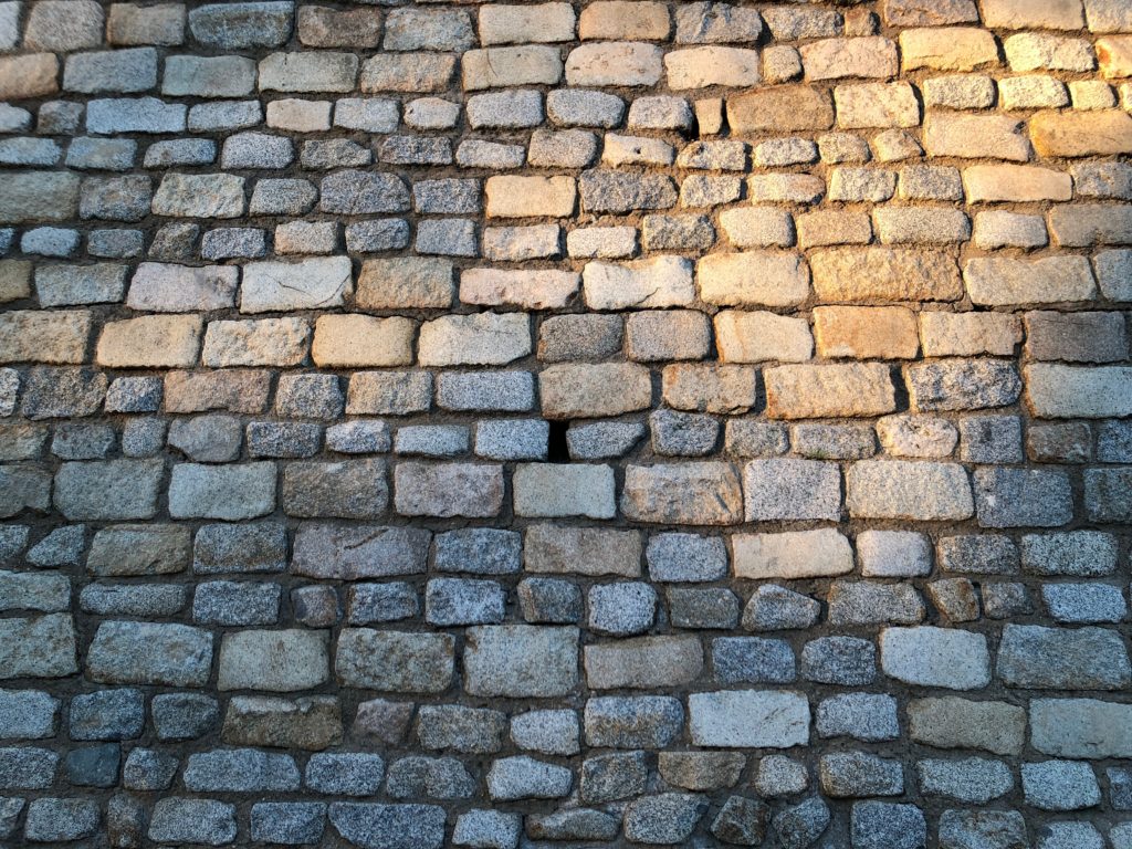 The rays of the sunset light up a wall of odd bricks.