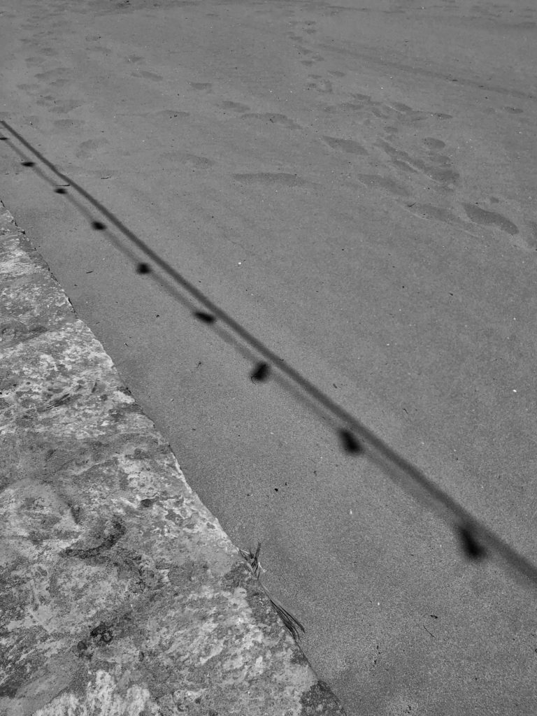 The shadow of garland lights cast on the beach sand.