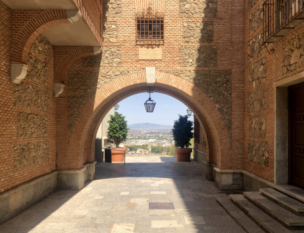 An arch with a view over the city of Murcia in the background, flanked by trees.